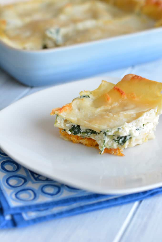 A slice of creamy butternut squash lasagna stuffed with three cheeses and fresh spinach on a white plate.