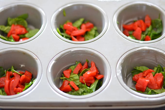 Roasted pepper and chopped spinach inside muffin cups.