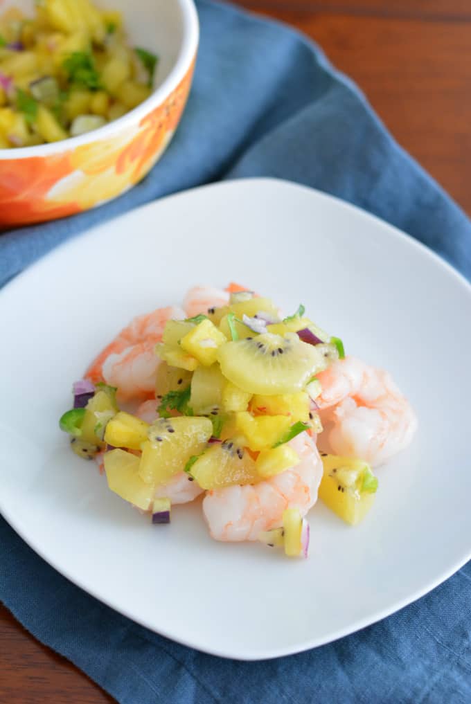 Kiwi pineapple fruit salsa on top of shrimp on a white plate.