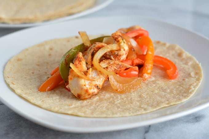 Chicken, onions, and pepper on top of a whole wheat fajitas shell.