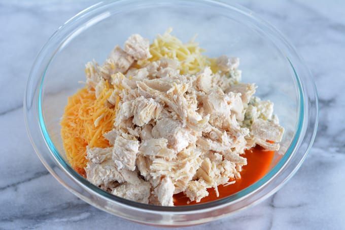 A bowl with chicken, cheese, and hot sauce to make baked buffalo chicken dip.