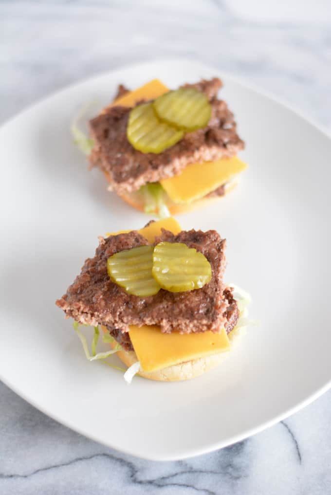 Open faced cheese burger with pickles on top.