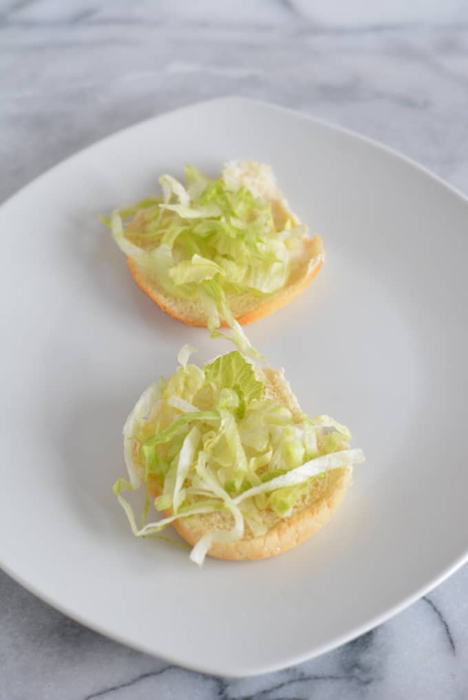 Lettuce on the bottom of a hamburger bun.