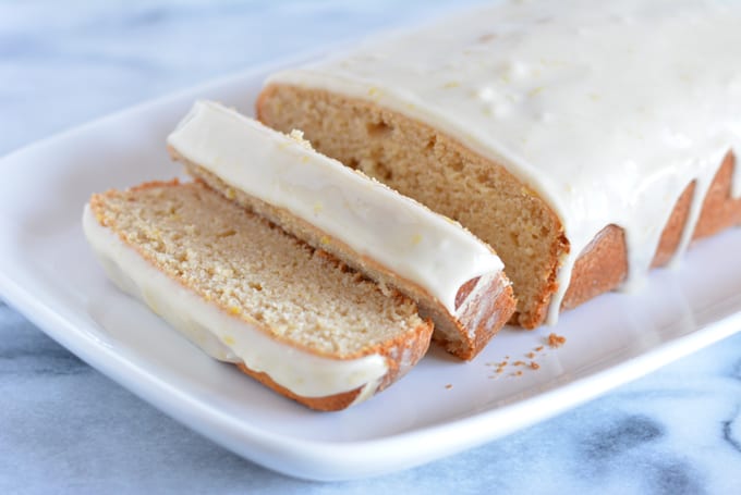 A glazed lemon loaf sliced on a white plate.