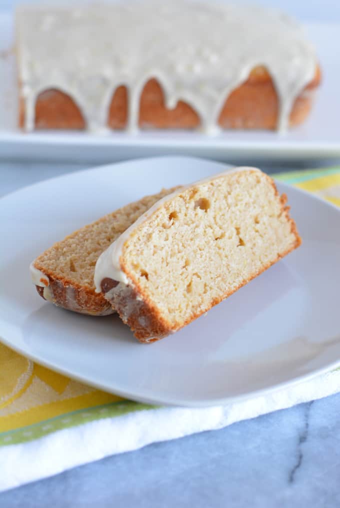 Two slices of a glazed lemon loaf on a white plate.