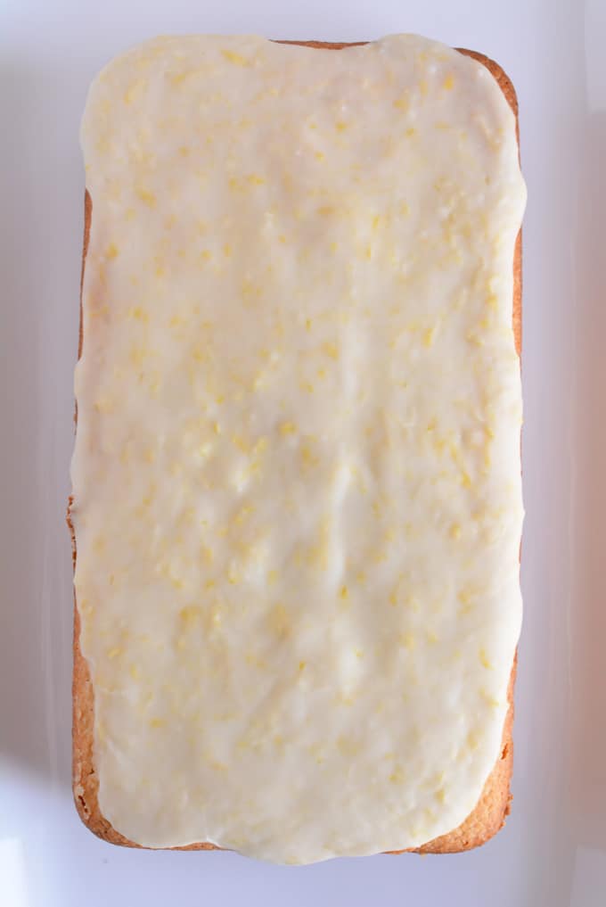 A glazed lemon loaf not sliced on a white plate.